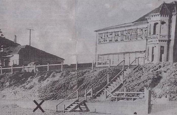 Old black and white photo of a coastal house and beach steps, linked to the world's most baffling unsolved mysteries.