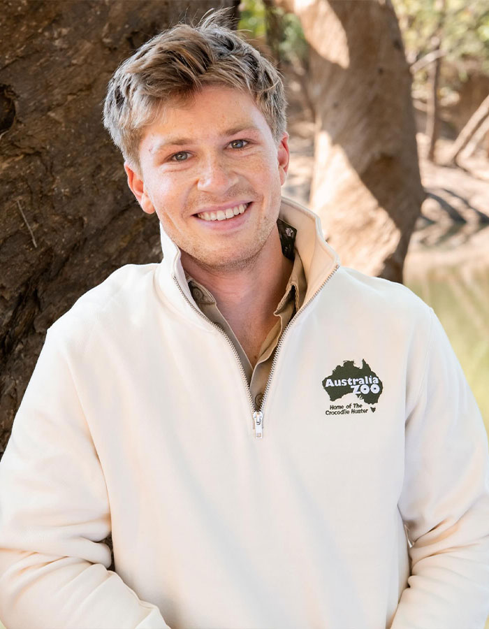 Young man smiling outdoors wearing Australia Zoo jacket, related to Steve Irwin’s surprisingly small fortune left to children Robert and Bindi. - 6