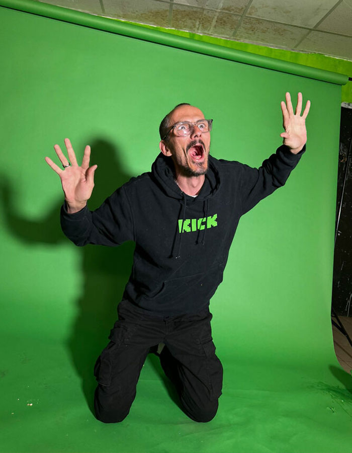 Streamer in a black hoodie posing dramatically against a green screen backdrop during a live on-air session. Streamer in a black hoodie posing dramatically against a green screen backdrop during a live on-air session.