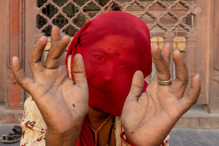 Woman in a red veil showing worn hands in a powerful street photo capturing the beauty of everyday life.