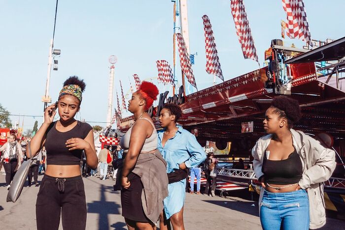 Four young women standing and talking near a colorful carnival ride in a powerful street photo capturing everyday life.