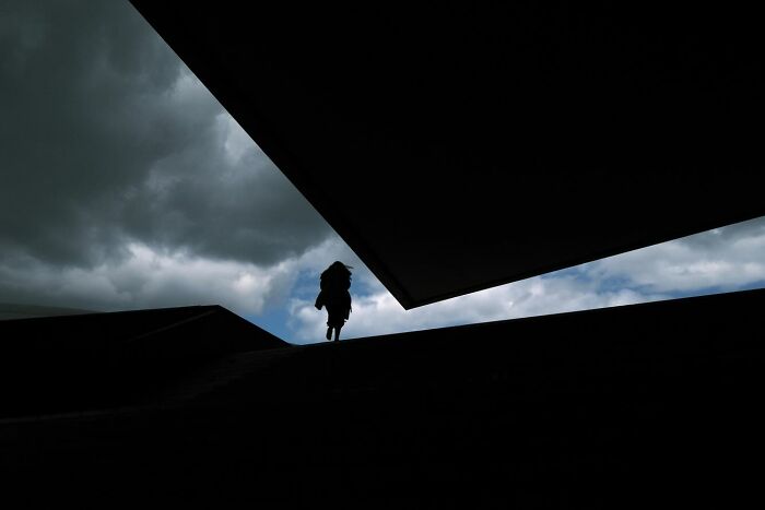Silhouette of a person walking on stairs under dramatic clouds in a powerful street photo capturing everyday life beauty.