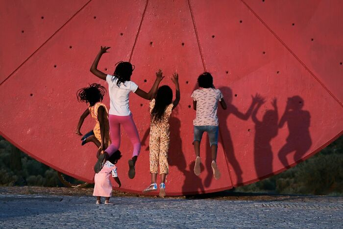 Children joyfully jumping in front of a large red wall, a powerful street photo capturing the beauty of everyday life.
