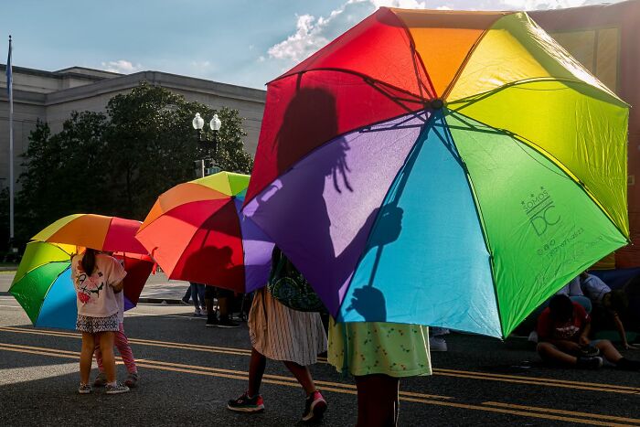Children holding colorful umbrellas on a sunny street, capturing powerful street photos that reveal the beauty of everyday life.