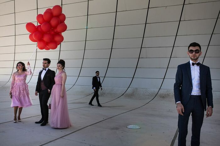 Group of young people dressed formally, with red balloons, captured in a powerful street photo showing everyday life beauty.