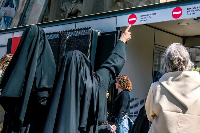 Two people in black cloaks pointing at a street sign with others gathered nearby in a powerful street photo.