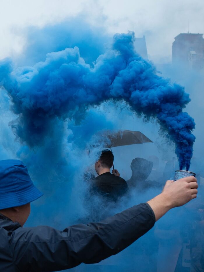 Person holding blue smoke flare in a street scene, capturing powerful street photos that reveal everyday life beauty.