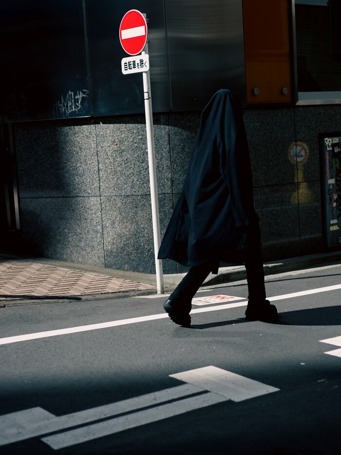Person dressed in black walking past no-entry sign on street, powerful street photo capturing the beauty of everyday life.
