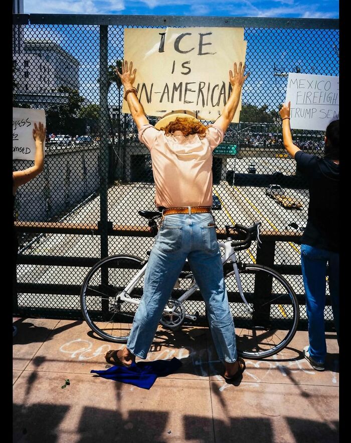 Person holding a protest sign on a fence next to a bicycle, captured in a powerful street photo of everyday life.