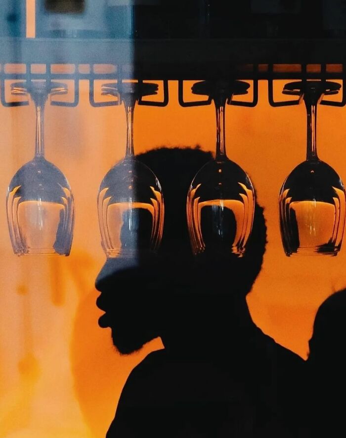 Silhouette of a man behind hanging wine glasses, capturing a powerful street photo revealing everyday life’s beauty.