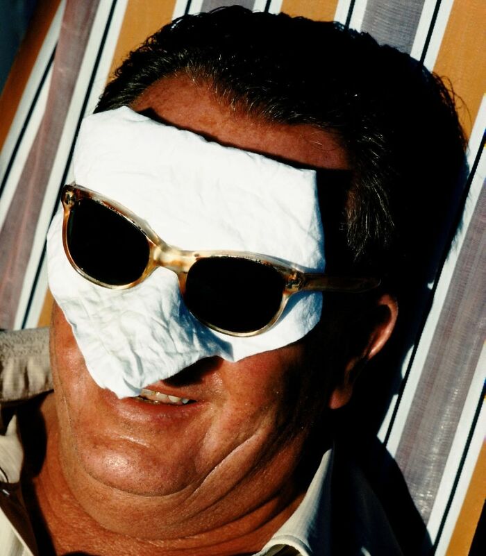 Man resting with sunglasses over a white cloth on his face in a powerful street photo capturing everyday life.