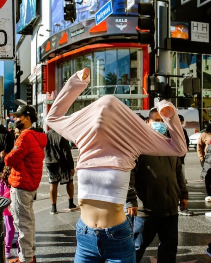 Person pulling a shirt over their head on a busy city street, capturing spontaneous moments in powerful street photos.