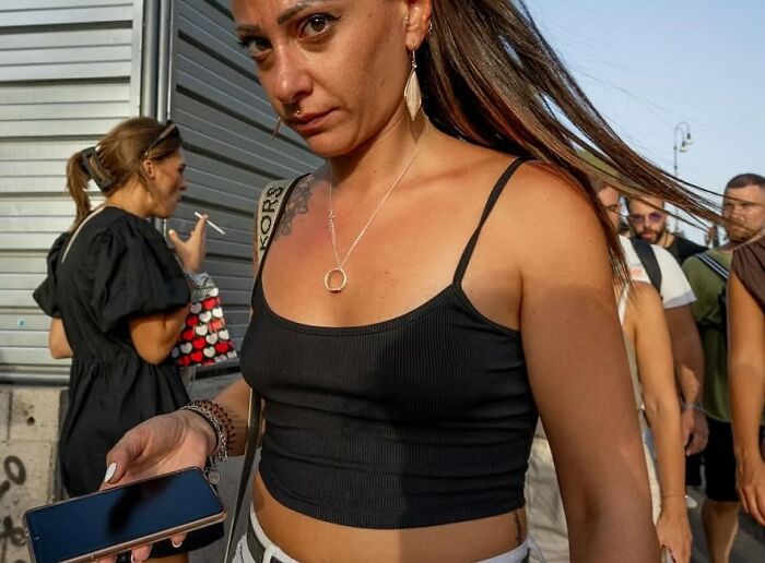 Woman with piercing and jewelry holding a phone outdoors, captured in a powerful street photo showing everyday life beauty.