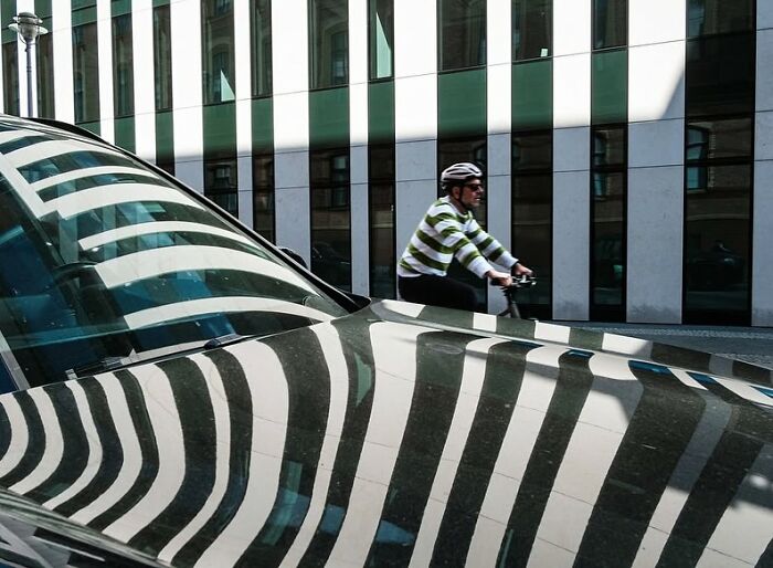 Cyclist passing by a building, with striking reflections creating powerful street photos of everyday life.