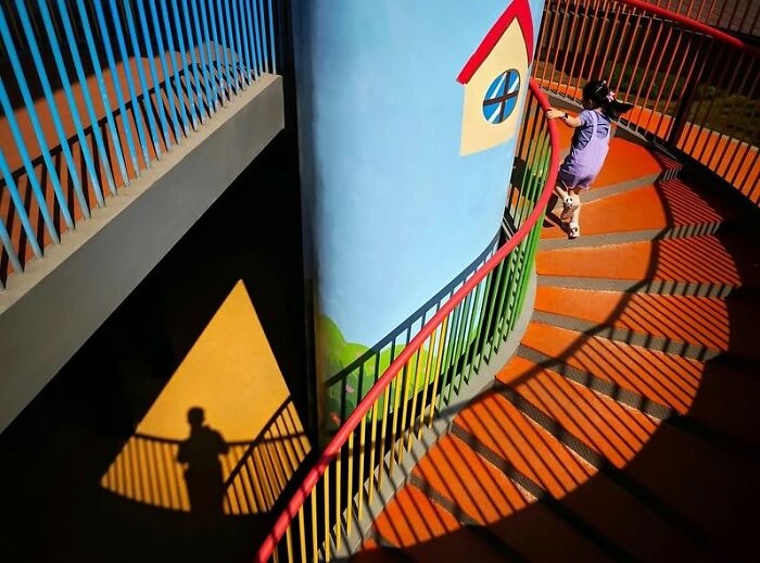 Colorful street photo of a child climbing a spiral staircase with strong shadows revealing everyday life beauty.