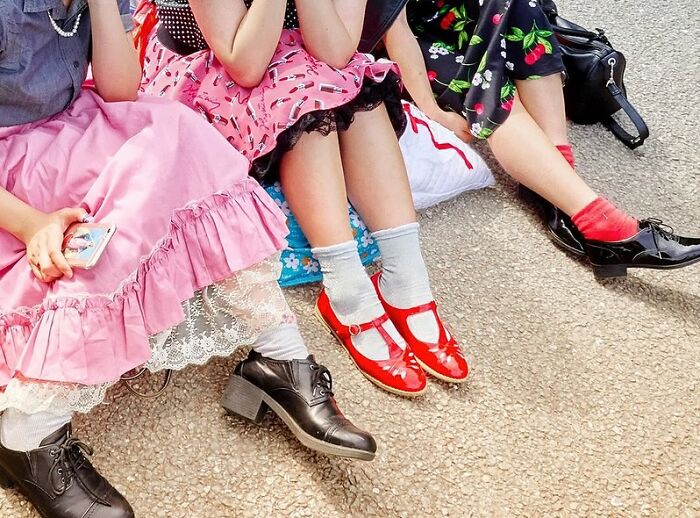 Three women sitting on the ground wearing colorful vintage dresses and shoes in a powerful street photo capturing everyday life.