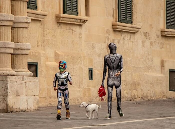 Two people in futuristic outfits walking a dog on a quiet street, showing powerful street photos of everyday life.