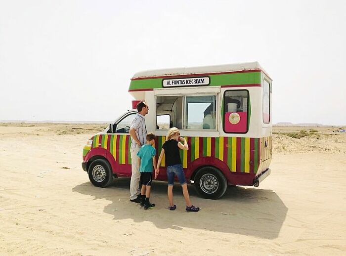 A family waiting at a colorful ice cream truck in a sandy open area, capturing the beauty of everyday life in street photos.