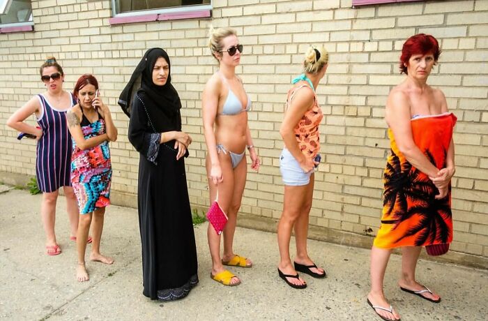 A diverse group of women standing in line against a brick wall, captured in a powerful street photo of everyday life.
