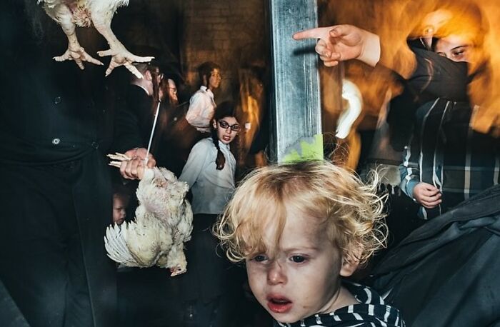 Young child in a crowded street scene, with people and poultry, captured in a powerful street photo revealing everyday life.