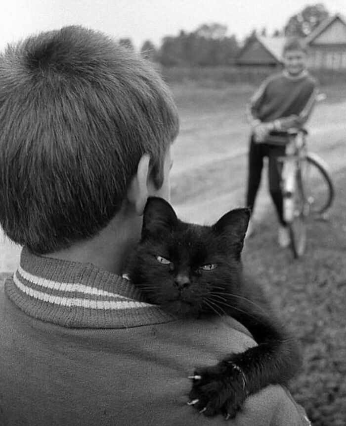 Black and white street photo of a boy holding a black cat, capturing the beauty of everyday life outdoors.