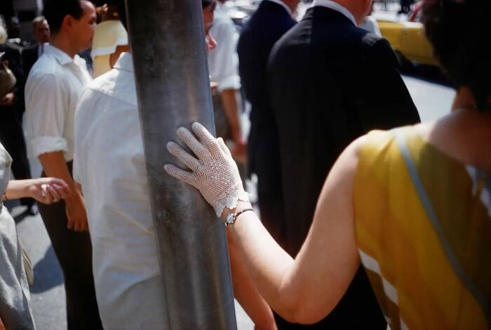 Woman wearing vintage lace glove touching a street pole in a busy urban scene, captured in powerful street photos.
