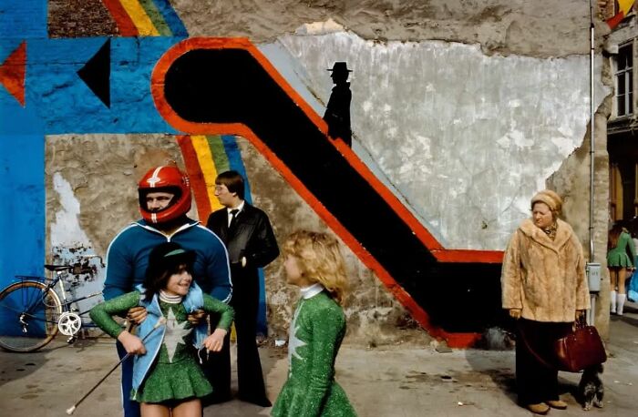 Street photo of people in colorful outfits posing near a wall with vibrant mural, capturing the beauty of everyday life.