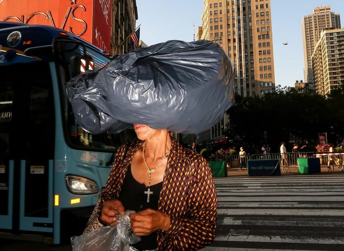 Woman crossing city street with a large plastic bag on her head in a powerful street photo capturing everyday life moments.