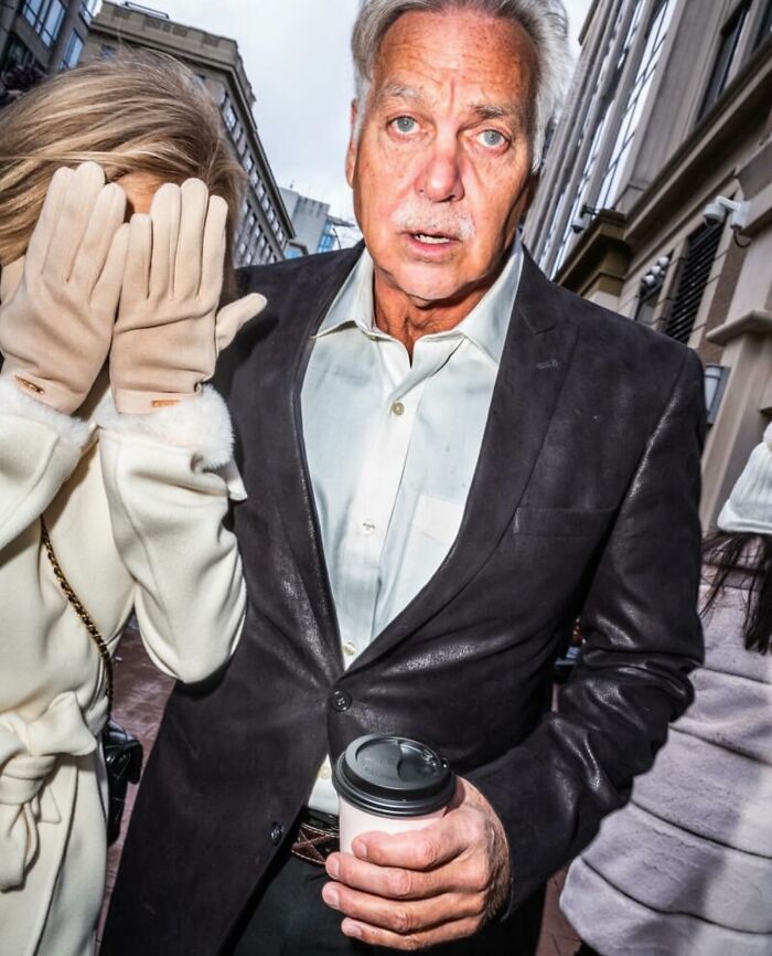 Man holding a coffee cup and woman covering face with gloves in a powerful street photo capturing everyday life.