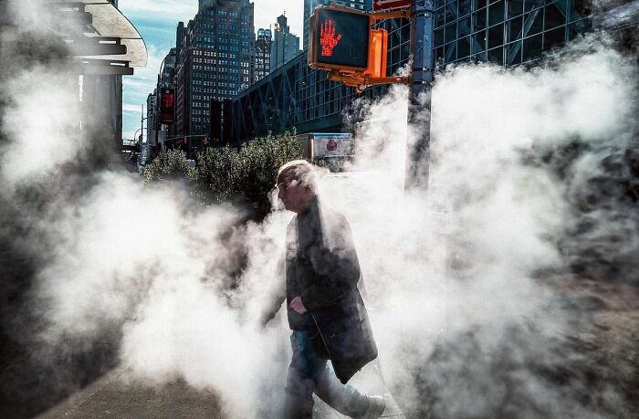 Man walking through steam on a city street beneath a stop hand signal, a powerful street photo capturing everyday life.