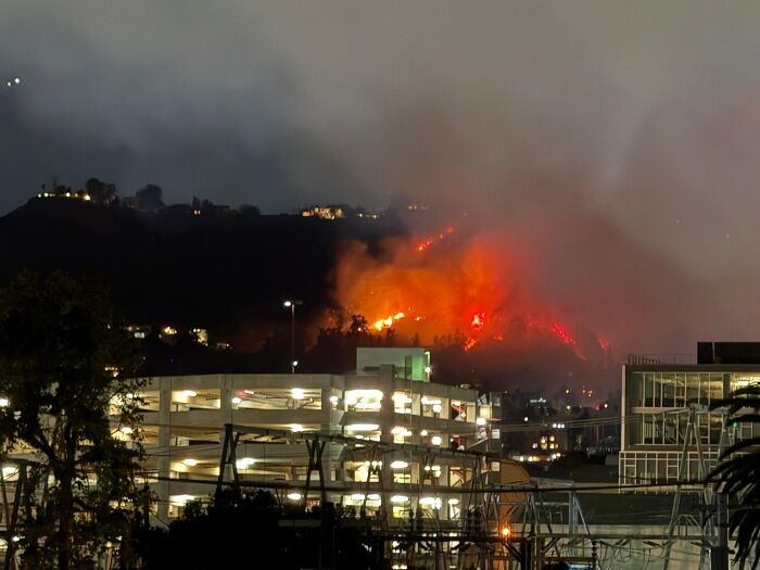Nighttime cityscape with a large wildfire burning on a hillside, illustrating headlines that rocked the world in 2025.