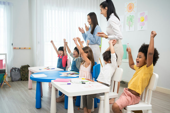 First grade kids cheering with teacher in classroom during a fun song about private parts education. First grade kids cheering with teacher in classroom during a fun song about private parts education.