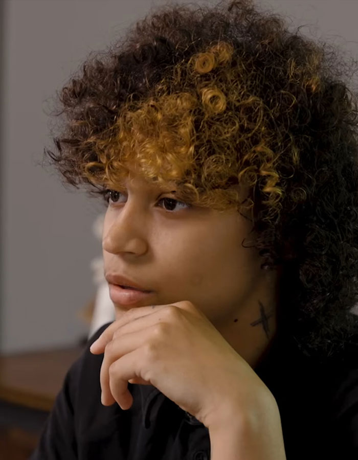 Teen with curly hair and thoughtful expression, highlighting experience of restaurant server forcing gender proof.