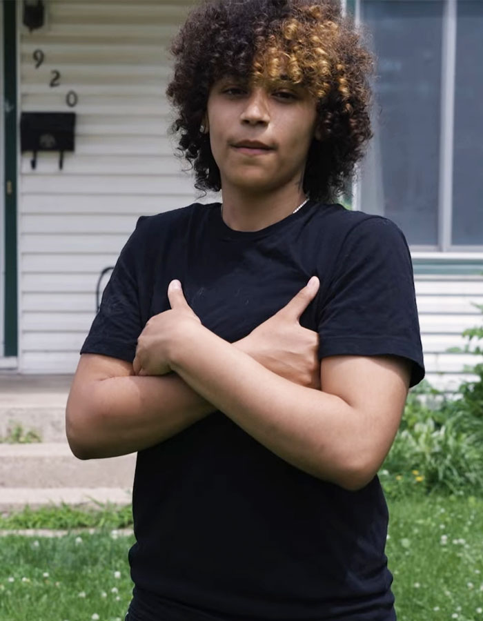 Teen standing outside home with arms crossed, related to restaurant server forcing her to prove gender in altercation.
