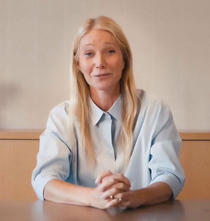 Blonde woman sitting at a table, speaking in a casual setting, related to Chris Martin cheating scandal controversy.