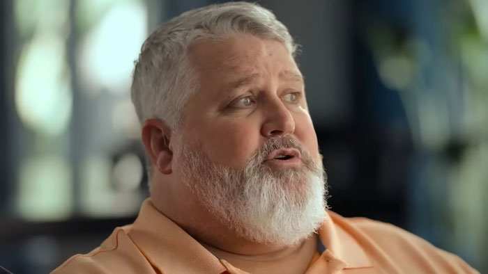 Middle-aged man with gray hair and beard speaking in an interview about The Biggest Loser and PTSD effects.