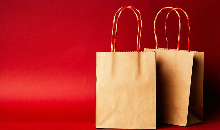 Two plain brown paper shopping bags with twisted handles against a solid red background representing then vs now scenarios.