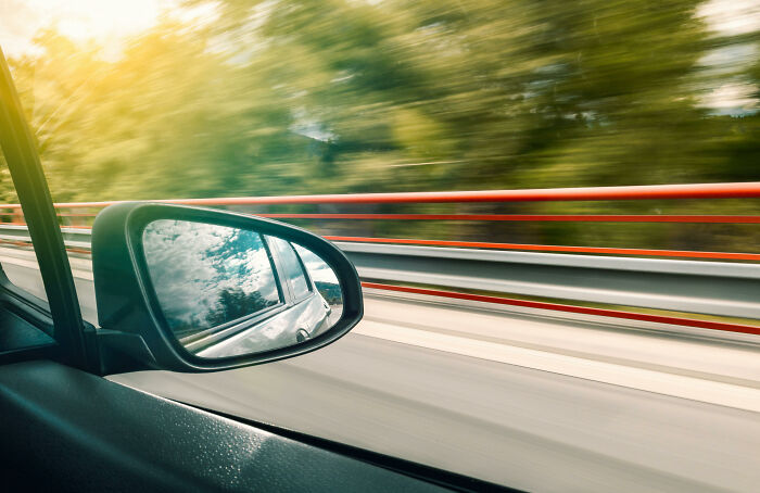 Car side mirror reflecting sky on a fast-moving road, illustrating then vs now scenarios in motion and perspective.