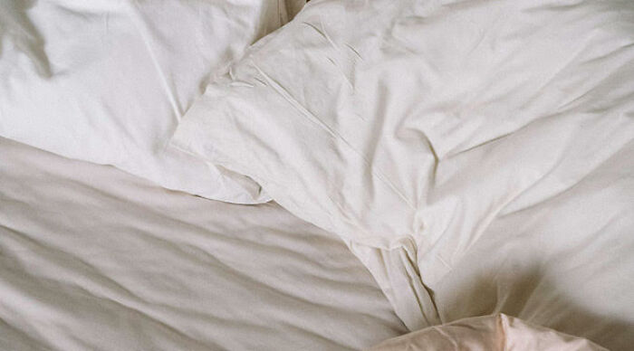 A messy white bed with wrinkled sheets and pillows illustrating then vs now scenarios of comfort and rest.