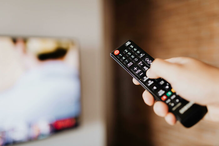 Hand holding a remote control pointing at a TV, illustrating then vs now scenarios in entertainment technology.