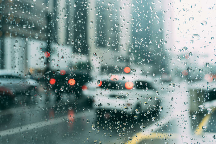 Raindrops on a window with blurred city traffic in the background, illustrating then vs now scenarios in urban settings.