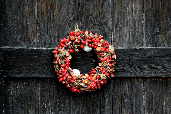 Decorative wreath with red berries, pine cones, and nuts hanging on a rustic wooden door highlighting then vs now scenarios.