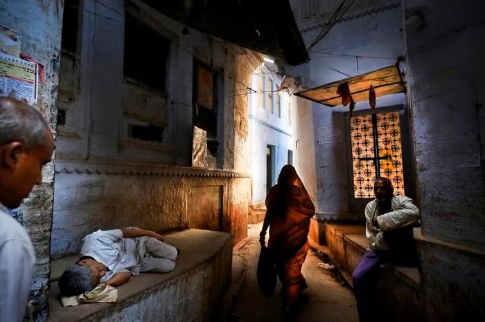 Man sleeping on stone bench and people walking in narrow alley captured in unforgettable street photos of everyday life art.
