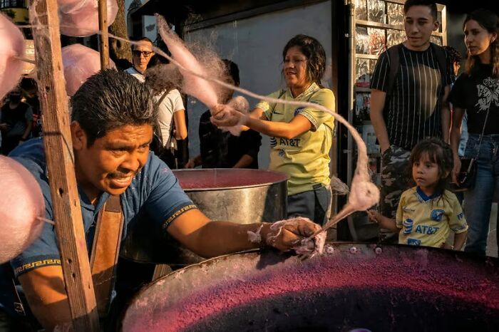 Man creating cotton candy at a street fair with onlookers, capturing unforgettable street photos of everyday life.