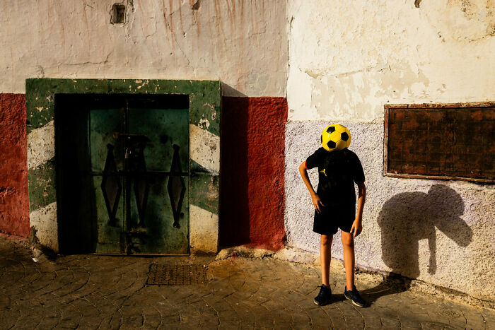Boy balancing a soccer ball on his head against a textured wall in an unforgettable street photo capturing everyday life.