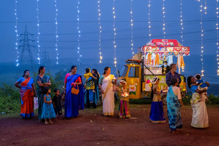Colorful street photo of people in traditional attire gathered near a decorated food truck under string lights at dusk