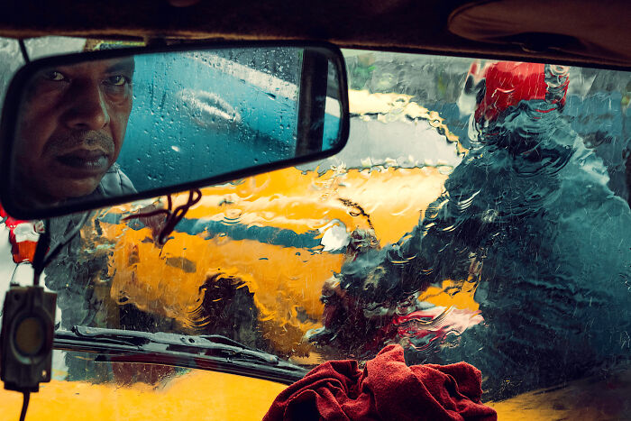 Man reflected in rearview mirror of a car with rain on the window, captured in unforgettable street photos of everyday life.