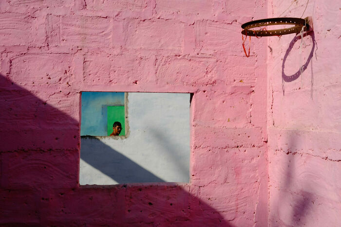 Man peering through layered colorful walls near a basketball hoop in an artistic street photo capturing everyday life.
