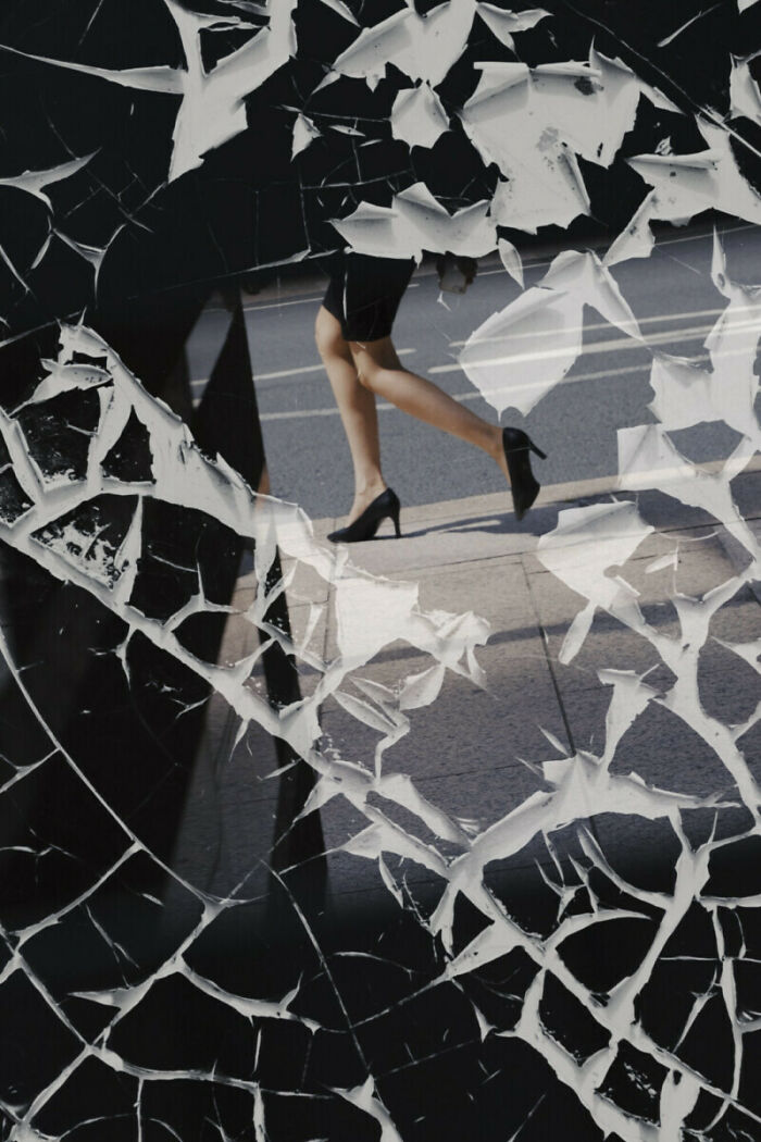 Street photo of a woman in high heels walking on a city sidewalk captured through shattered glass artfully.