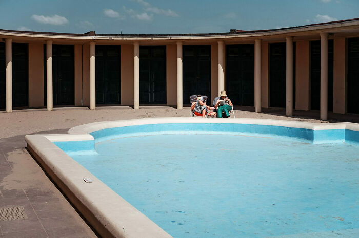 Two people relaxing by an empty pool in a courtyard, capturing unforgettable street photos of everyday life.